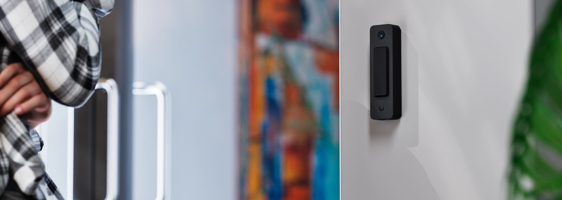 Ubiquiti Doorbell Lite zamontowane na białej ścianie, z widoczny tłem i lekką rozmytą barwą z kolorowymi obrazkami