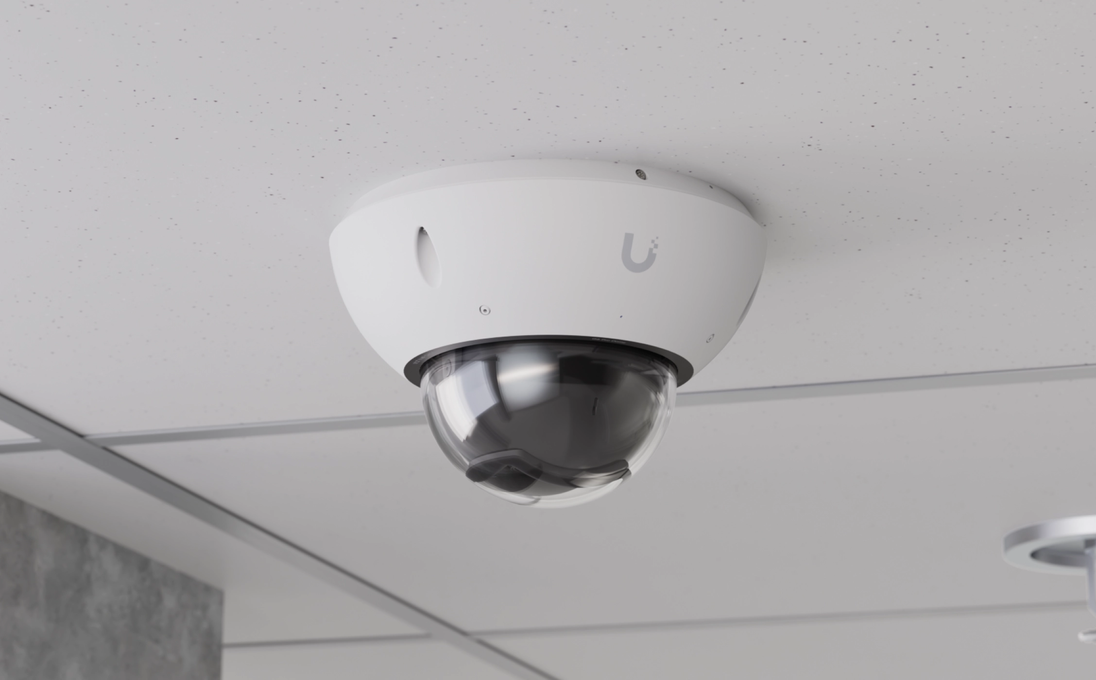 Kamera Ubiquiti UVC-G6 Pro Dome zamontowana w suficie podwieszanym, biała obudowa i przyciemniana kopuła, neutralne biurowe tło