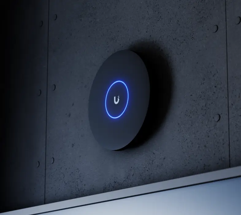 Czarny punkt dostępowy Ubiquiti U7 Pro XG świecący niebieskim pierścieniem LED, zamontowany na betonowej ścianie