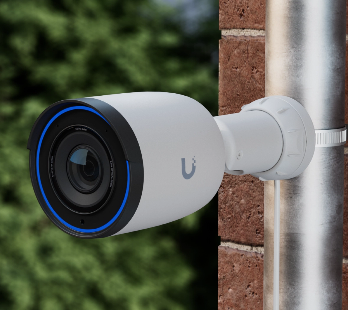 Kamera Ubiquiti UVC-G6 Pro Bullet zamontowana na rurze, z niebieskim pierścieniem LED wokół obiektywu, na tle zieleni