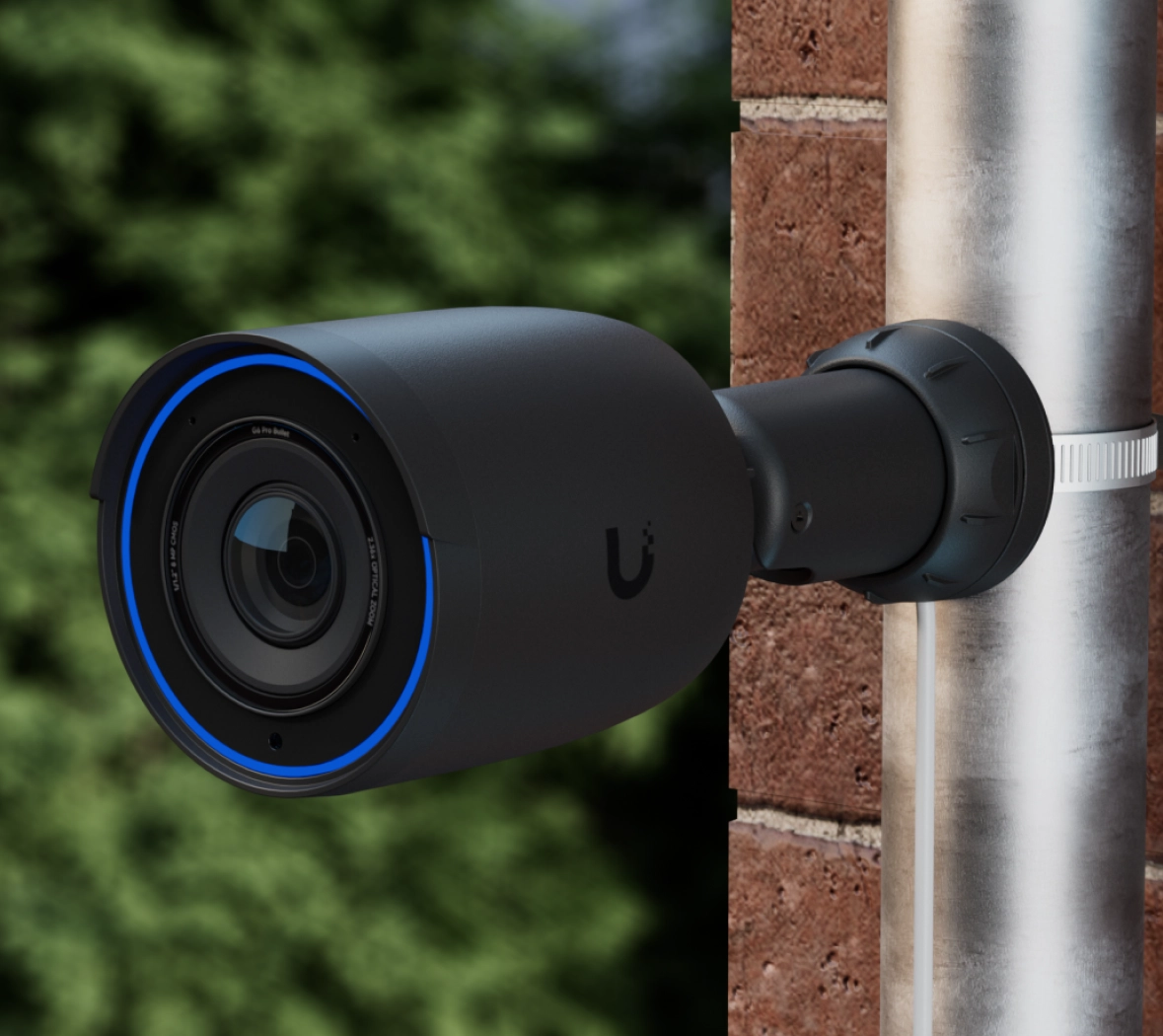 Kamera Ubiquiti UVC-G6 Pro Bullet zamontowana na rurze, z niebieskim pierścieniem LED wokół obiektywu, na tle zieleni